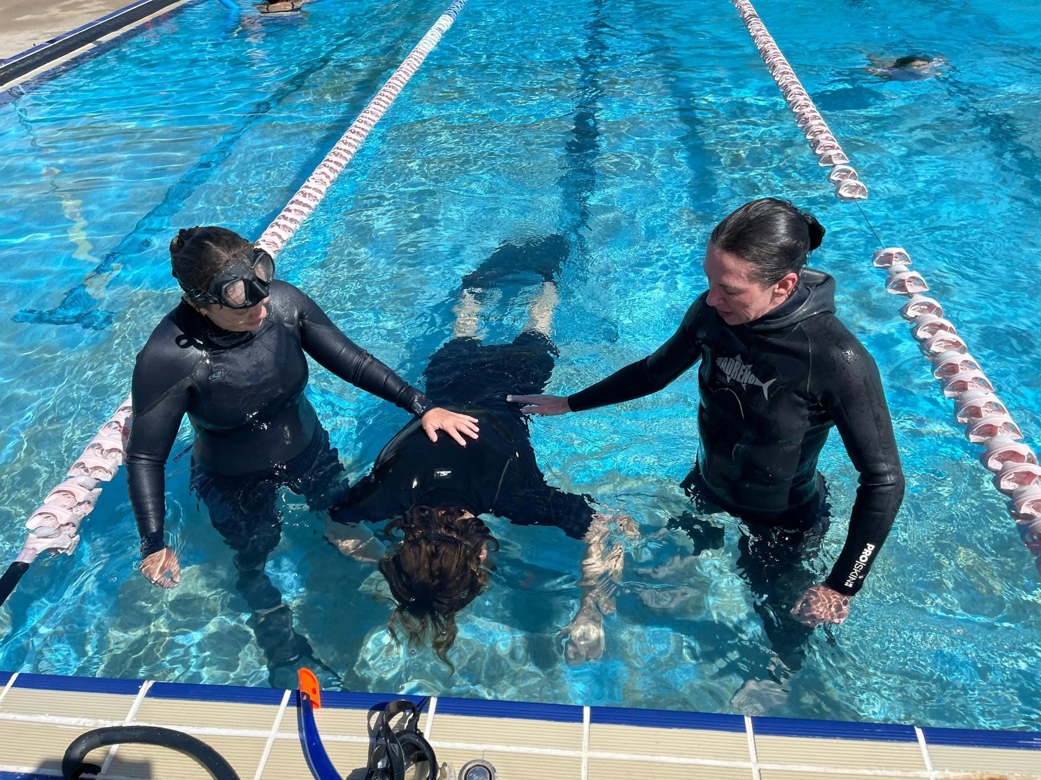 Deux encadrantes accompagnent une pratiquante lors d’un exercice d’apnée en piscine.